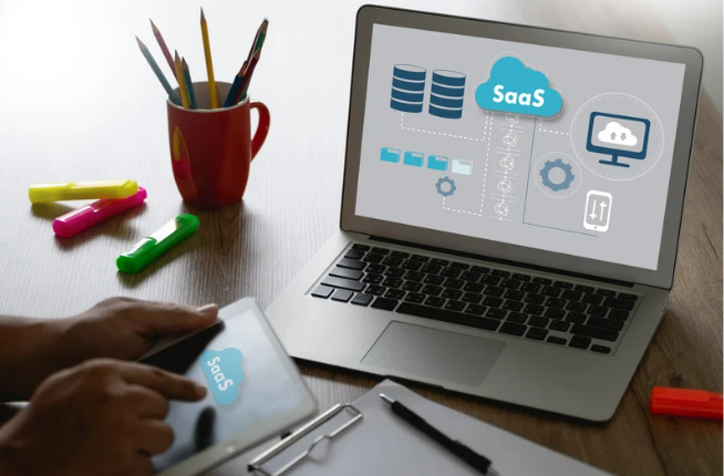 Laptop showing HR SaaS platform architecture diagram with cloud icons and user interfaces, alongside planning materials on a desk