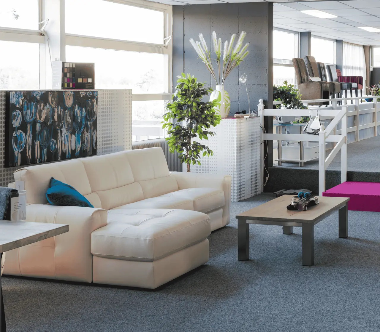 Modern furniture showroom displaying white leather sectional sofa with blue accent pillows and contemporary art