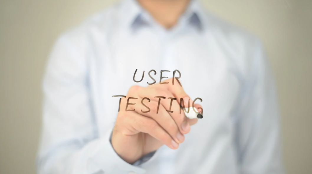 Person writing 'USER TESTING' on a transparent board with a marker